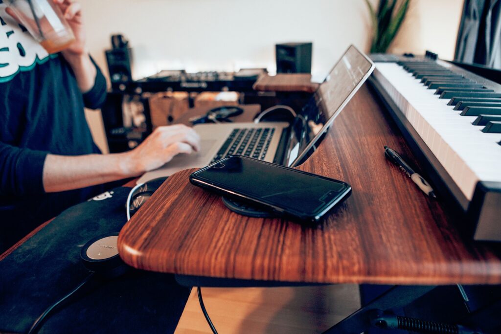 Person sitting at a desk in their home office with a laptop, phone, and keyboard on it.